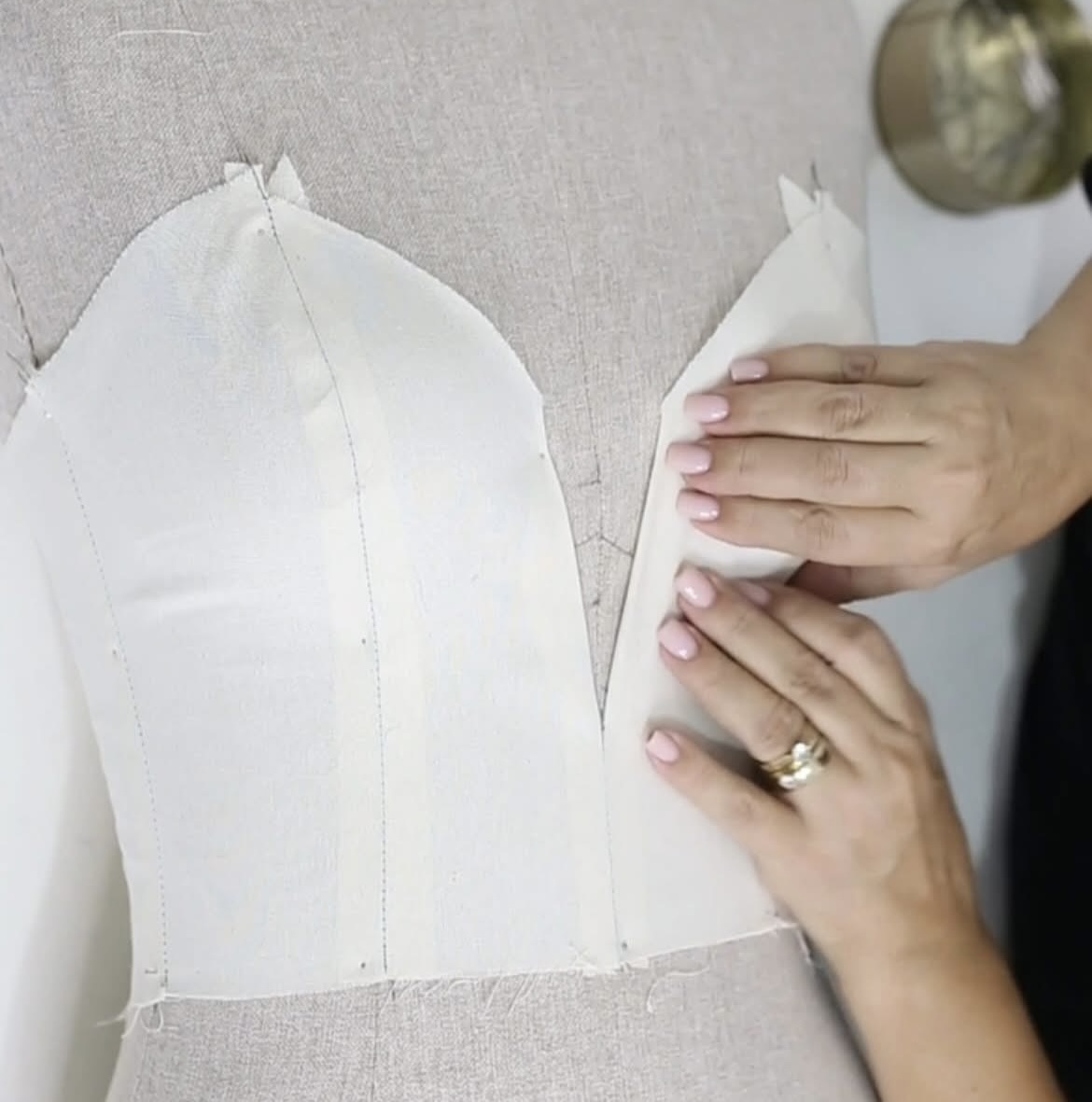 Hands positioning white fabric on a dress form.